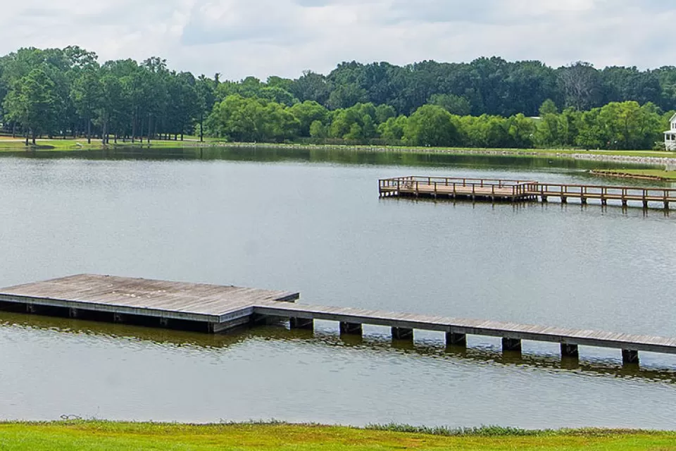 View of docks on lake surrounded by green trees and lawns with one white house at right